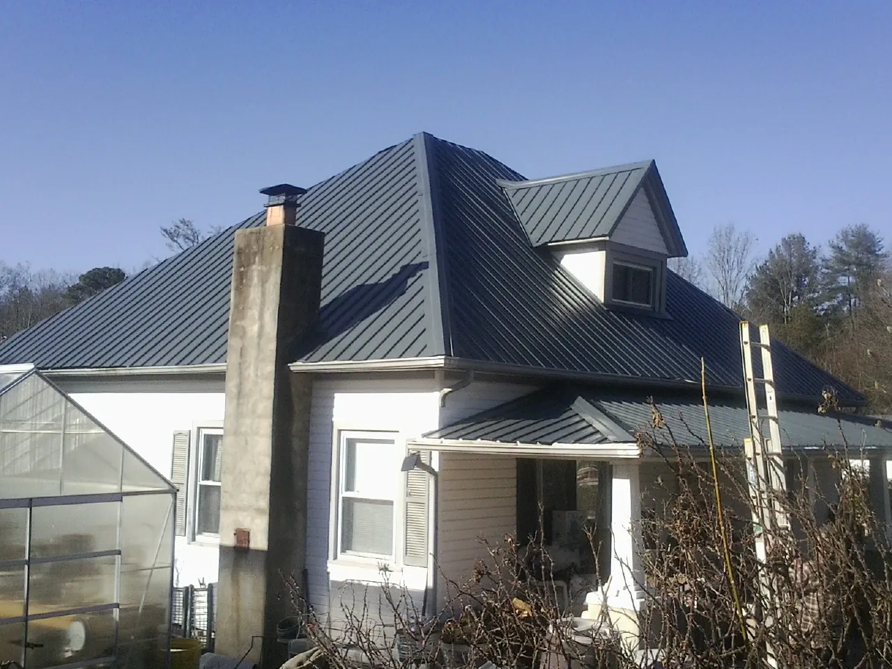 Dark blue standing seam metal roof on a white farmhouse with dormer — Slate & Tile Roof Repair by Roofing Brothers in Aliceville