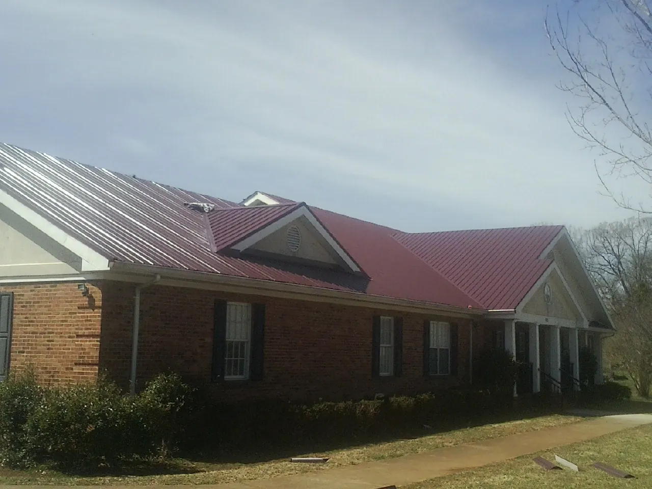 Red metal roof with gabled entries on a long brick building, from a Hail Damage Roof Repair job in Aliceville