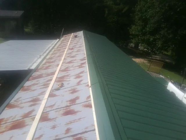Old rusted panels beside newly installed green metal roofing — Wind Damage Roof Repair by Roofing Brothers in Aliceville