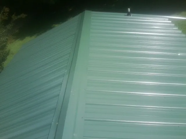 New green metal panels meeting at the ridge of a roof — Flat Roof Repair work by our crew in Aliceville