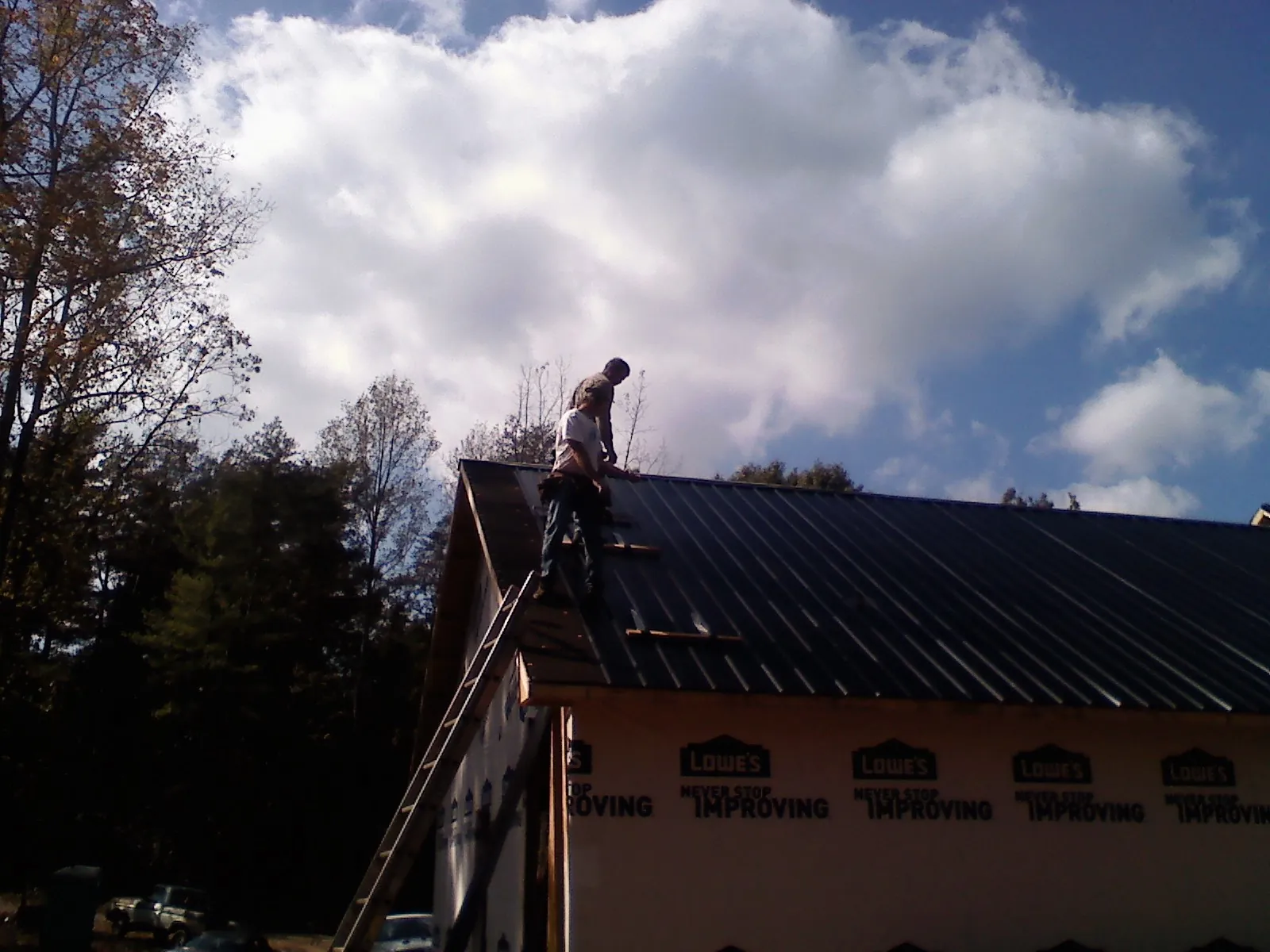 Roofer fastening dark metal panels high against a cloudy sky, from a Roof Inspection job in Aliceville