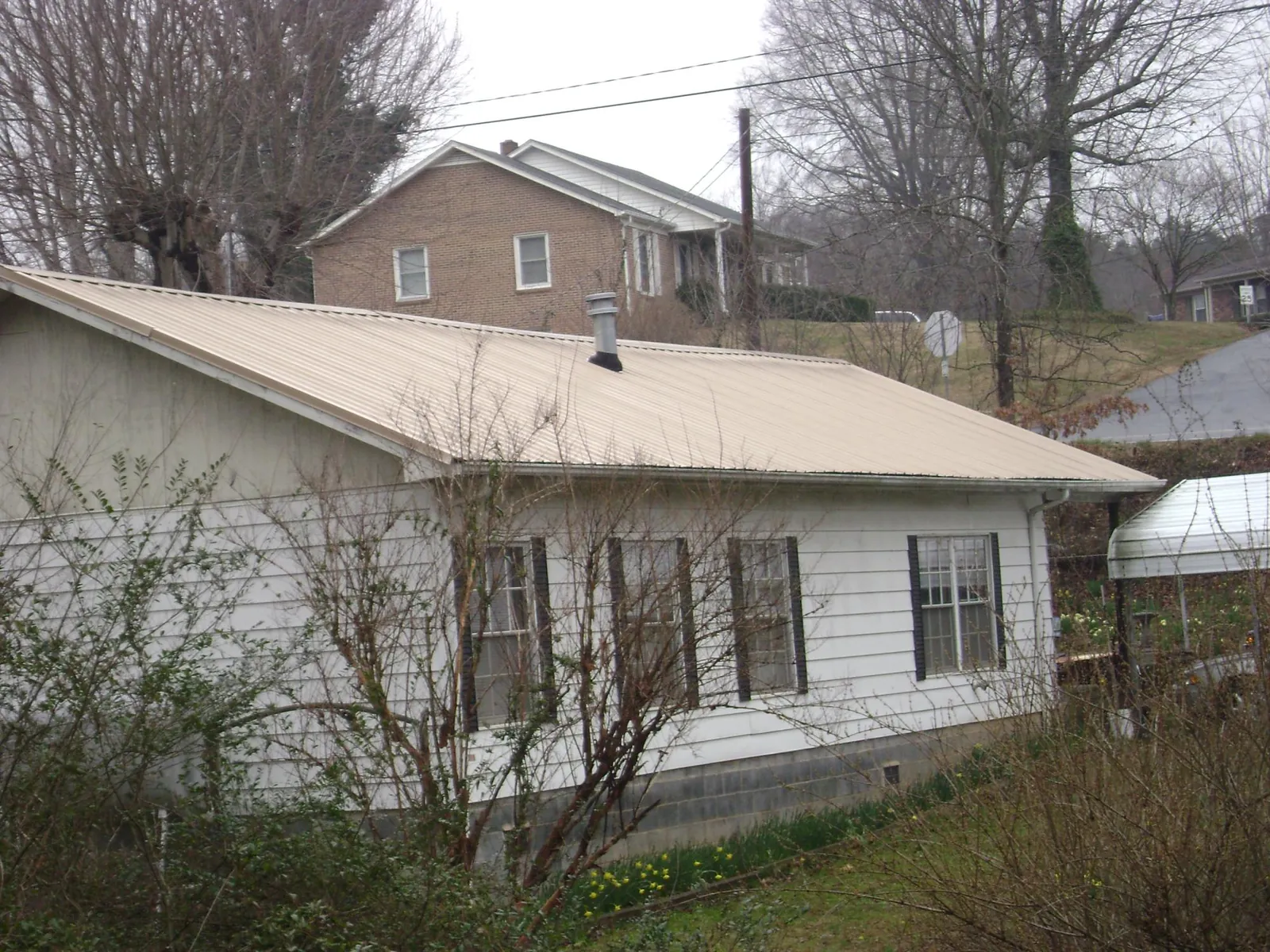 Tan metal roof on a white sided house set into a hillside — Commercial Roofing by Roofing Brothers in Aliceville