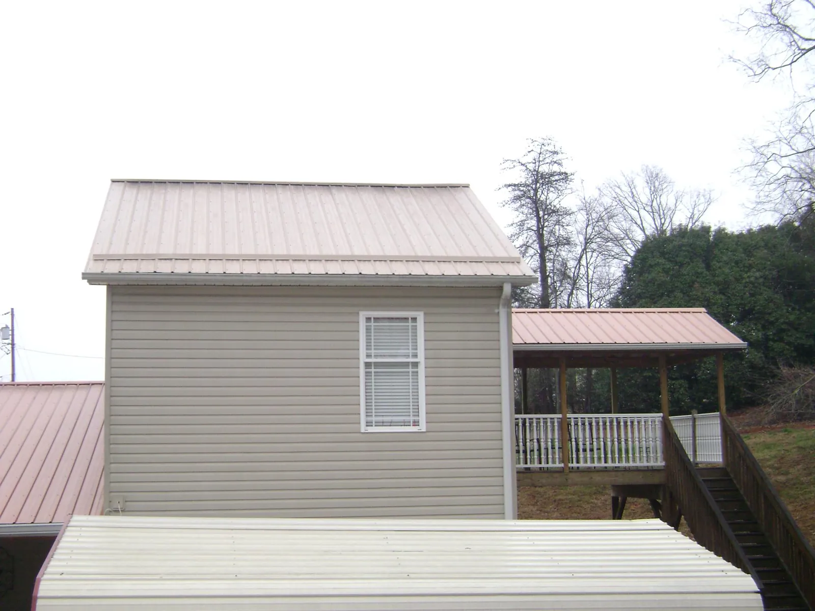 Tan metal roofs on a two story addition and attached porch, from a Roof Replacement job in Aliceville